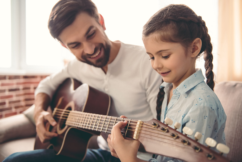 father teaching his daughter to play the guitar